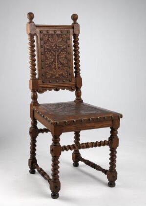  An intricate dark brown antique chair with a tall, carved backrest featuring a symmetrical floral pattern and supporting turned legs connected by spiral stretchers, illustrating expert craftsmanship.