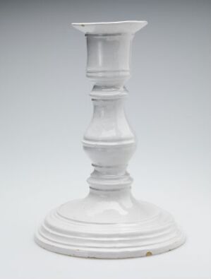  A white porcelain candlestick holder with a broad base, sculptural bulges, and a flared rim, displayed against a light grey background.