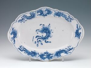  An oval-shaped, blue and white porcelain platter featuring a central cobalt blue dragon design and a scalloped edge with a matching blue motif. The platter rests against a neutral gray background, emphasizing the vibrancy and detail of the blue patterning.