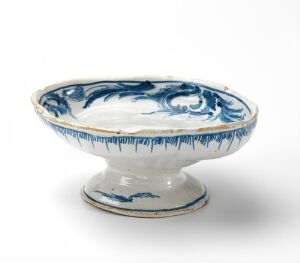  A white-glazed fajanse bowl with cobalt blue hand-painted decoration, created by Herrebøe Fajansefabrikk, featuring a traditional design on both the bowl and its pedestal base.