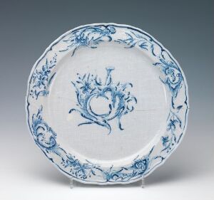  An off-white faience plate with hand-painted bianco sopra bianco details and cobalt blue floral and leaf motifs, exhibiting a traditional, ornate style with a glossy finish; artist unknown.