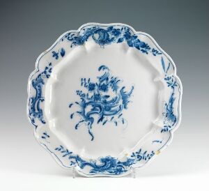  A round, shallow plate made by Herrebøe Fajansefabrikk, titled "Rundt formed fladt Fad", featuring wheel-thrown, white-glazed faience with hand-painted cobalt blue decorative elements, likely of a floral or traditional pattern, against a white background.