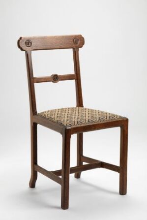  A traditional wooden chair with a woven seat, featuring a straight backrest with a decorative top rail, set against a light gray background.