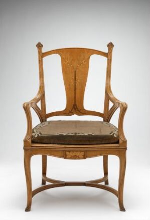  An ornate wooden chair with a warm golden-brown frame featuring a tall, curved backrest with intricate designs and a cushioned seat with a floral-patterned fabric. The chair stands against a light gray background.