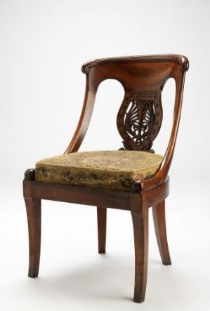  A classic wooden chair with a square-shaped upholstered seat in a muted gold color and a delicately carved openwork design on the backrest, set against a light background.