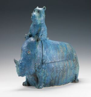  A whimsical stoneware art piece by Finn Mauritz Hald, entitled "Uten tittel," featuring a stylized rhino with a bear seated on its back, glazed in a variety of blue tones that accentuate the work's textures and playful essence.