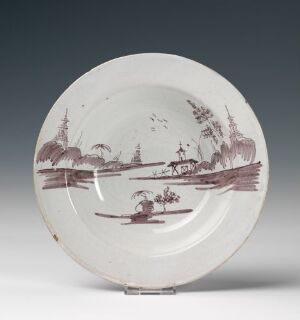  Antique circular plate with a shallow concave surface displaying a hand-painted landscape in reddish-brown, depicting Eastern-style buildings, stylized trees, a small boat, and a serene body of water, set against an off-white background.