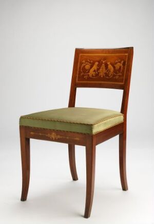  An antique-style wooden chair with square legs and a cushioned seat upholstered in faded olive green, featuring an intricately carved backrest panel with a classical scene. The chair stands against a light gray background.