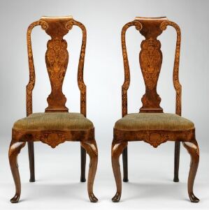 
 A pair of antique wooden chairs with intricate grain patterns and a glossy finish, featuring ornate vase-shaped backrests and cabriole legs, upholstered with faded mustard-colored fabric with a dark floral pattern.