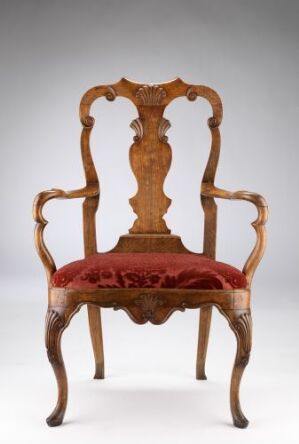  An antique wooden armchair with ornate carvings and red upholstered seat, set against a neutral gray background.