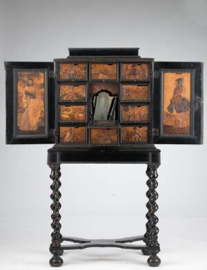  An antique wooden cabinet with decorative panels and drawers in various shades of brown, set atop a table with turned black legs.