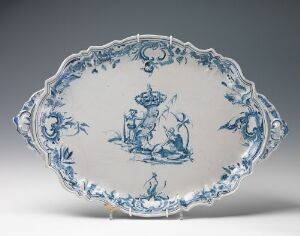  An oval-shaped porcelain platter with scalloped edges, displaying a white and cobalt blue painted scene with figures in a pastoral landscape, surrounded by intricate floral and scroll designs.