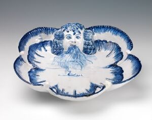  An antique porcelain bowl with a central winged cherub design in relief, surrounded by intricate blue patterns on a white background. The edges of the bowl are scalloped, resembling feathers.