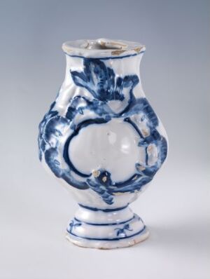  A white-glazed earthenware vessel with hand-painted cobalt blue floral decoration by Herrebøe Fajansefabrikk. The vessel has a curvaceous shape with a broad central body narrowing at the neck and base.