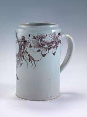  A pale blue cylindrical ceramic mug with intricate purple-brown vine-like patterns on its side and a simple handle, set against a neutral gray background.