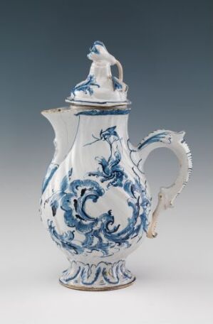  An exquisite white-glazed faience pitcher with hand-painted cobalt blue decorations, designed by Herrebøe Fajansefabrikk, featuring an ornate handle and a figural lid. The porcelain piece is cast and exhibits classic floral motifs and patterns, indicative of traditional ceramic artistry.