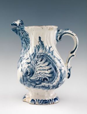  An oval-shaped, white-glazed earthenware jug, entitled "Oval Formed Melke-Kande" by Herrebøe Fajansefabrikk, adorned with hand-painted cobalt blue decorative motifs, including a stylized peacock, with a graceful handle and three small rounded feet.