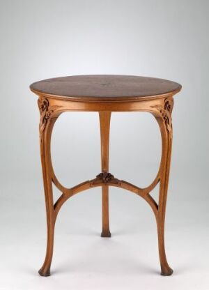  An Art Nouveau style wooden table with a round top and ornate, curved legs against a neutral background.