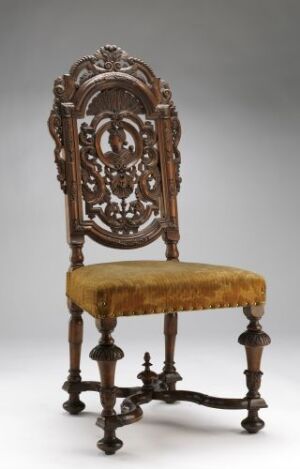  An intricately carved antique wooden chair with a tall, decorative backrest and plush golden-yellow upholstered seat, set against a light grey background.