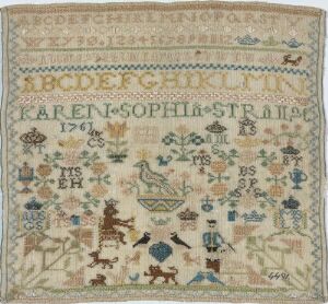  An antique sampler embroidered with alphabets, the name "KAREN SOPHIA STRAIJER," the year "1791," and various motifs including plants and animals, in a color palette of blues, greens, reds, browns, and yellows on a faded beige fabric.