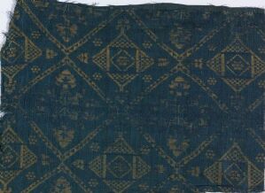  A fragment of aged textile with an intricate geometric pattern in golden and bronze on a dark blue background, with slightly frayed edges, suggesting historical or vintage origins.