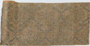  A rectangular piece of aged fabric with a faded pattern of interconnected almond shapes filled with intricate floral designs in muted brown, green, blue, and red tones on a light brown background. The piece appears historical with slightly frayed edges.