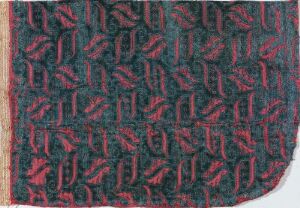  Textured fabric with a dark teal background and repeating pattern of stylized pinkish-red leaf-like motifs, frayed edges visible on one side.