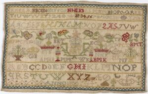  An aged, rectangular embroidery sampler with a beige background, featuring rows of embroidered letters, numbers, and various motifs such as flowers and birds in earthy tones, surrounded by decorative borders.