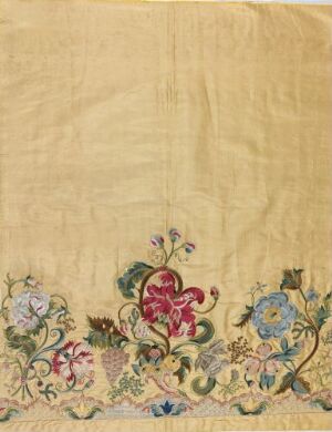  An antique textile with intricate floral embroidery in rich reds, blues, greens, and yellows on a warm beige background, showing signs of aging and detailed craftsmanship.