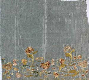  A piece of light grey fabric with a lower border embellished with stylized flowers in shades of gold, yellow, and copper, with green stems, creating an impressionist garden scene.