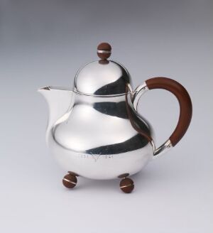  A modern silver teapot with a highly reflective surface and wooden handle, set on three small spherical feet. The teapot has a smooth, rounded body, a curved spout, and a spherical knob on the lid, presenting a sleek and contemporary design. (Artist name and title unknown)