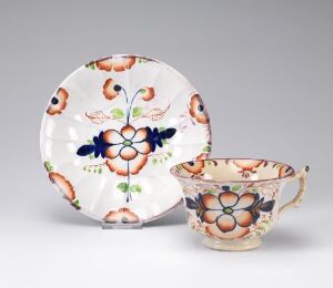  Porcelain plate and teacup set with bright floral motifs, featuring a cobalt blue central flower, surrounded by orange blooms with black outlines, and green leaves on an off-white background, demonstrating intricate design work and vibrant coloring.