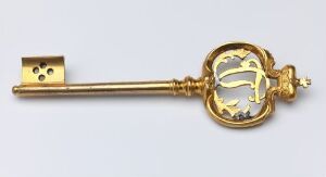  Gilded bronze key ("Kammerherrenøkkel") by an unidentified artist, featuring a circular head with openwork scroll-like patterns and a plain shaft ending in a rectangular bit with two cutouts, set against a light neutral background.