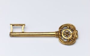  An antique gilded bronze key with elaborate openwork designs called "Kammerherrenøkkel," crafted by an unidentified artist, displayed against a neutral background.