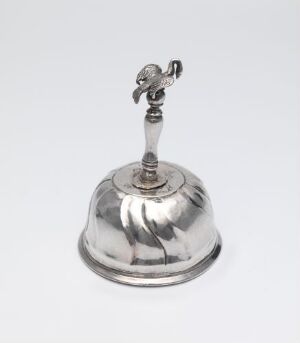  A silver service bell with a reflective dome-shaped bottom and a figurine handle, set against a light neutral background.