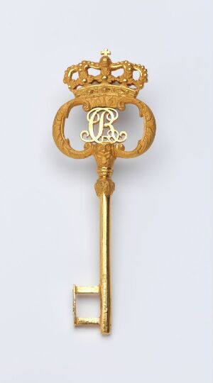  A "Kammerherrenøkkel" with elaborate bow featuring intertwined letters "C" and "R" within an ovate frame with a small crown on top, a textured shaft, and a simple geometric bit, made of gilded bronze set against a light-grey background.