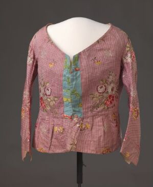 
 Antique-style blouse on a mannequin, featuring a dusty rose color with pastel floral embroidery and a contrasting sky blue placket.