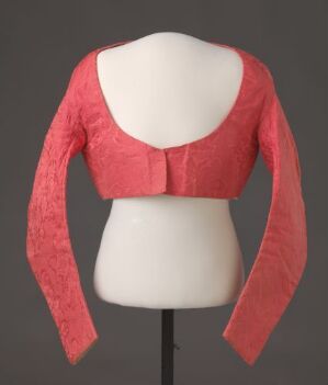  A mannequin torso displaying a coral-colored long-sleeved lace bolero jacket with a scoop neckline against a neutral gray background.