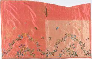  A piece of delicate fabric with a gradient from vibrant coral pink on the top to pale peach on the bottom, showcasing intricate floral patterns in the lower section with a small tear near the center.