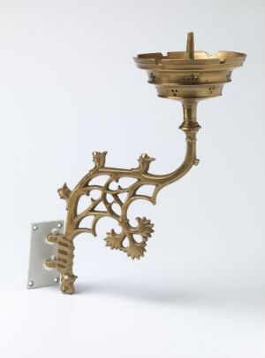  Antique bronze-colored wall-mounted candle holder with intricate vine and geometric patterns, against a light gray background.