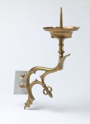  An antique brass wall sconce with intricate Baroque-style curves and a spike for holding a candle, against a light grey background.