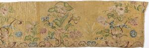  An ornate vintage floral tapestry segment on a beige background, featuring intricate green foliage and subtle blue and purple flowers, evoking a sense of antiquity and craftsmanship.