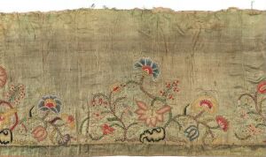  An aged textile or tapestry with a stylized floral pattern embroidered in shades of soft red, pale orange, faded green, and hints of blue on a light beige background. The craftsmanship suggests historical significance or decorative purpose. The artist name and title are unknown.