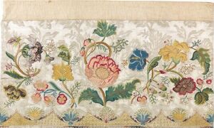  A textile featuring an ornate vintage floral pattern with a large central pink rose and surrounding flowers in shades of blue, yellow, and red, set against a cream-colored background with hints of aging. The design is dense with varied greenery and shows meticulous detail.