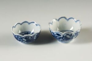  Two small blue and white patterned bowls with scalloped edges on a neutral surface, showcasing intricate East Asian floral designs.