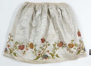  A full, pale-colored gathered skirt with an elastic waistband and drawstrings, adorned with scattered floral patterns in red, orange, yellow, and green on a white background.