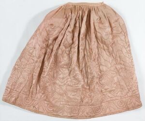  A quilted skirt in faded peach with intricate stitched floral patterns laid out on a light background.