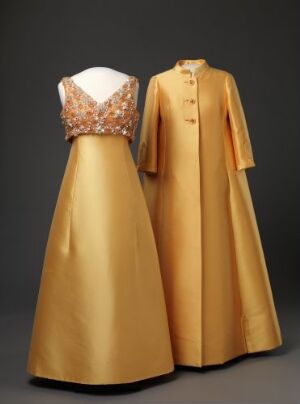  A two-piece formal ensemble displayed on mannequins, featuring a sleeveless golden dress with a sparkling embellished bodice and a full satin skirt, paired with a matching golden coat with long sleeves and a minimalist design, set against a dark gray background.