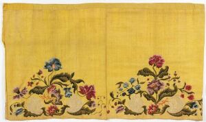  An ornate golden-yellow piece of textile, possibly silk, with intricate embroidery on both shorter ends, featuring lush green leaves and vibrant flowers in crimson, pink, blue, and lavender, accented by touches of azure and yellow, all set against a lustrous background.