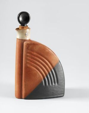  A terracotta-colored art deco style ceramic flask with a geometric ridged pattern on one side, transitioning from warm brown to charcoal grey. It features a gold-toned metallic cap and a black spherical stopper at the top. The object exudes a vintage elegance with its combination of matte, shiny, and polished textures.